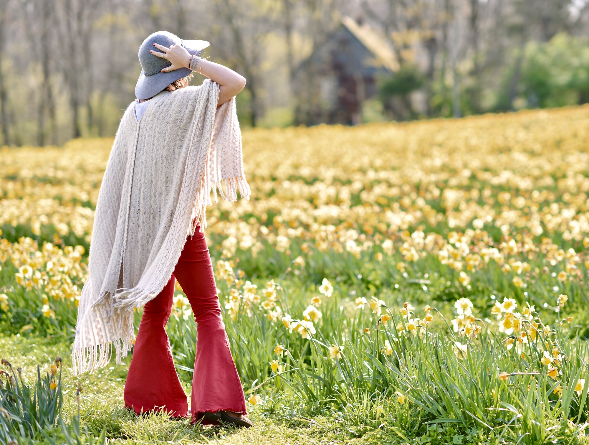 Beautiful young woman in red bell bottoms,boots & hat, overlooking a field of yellow Spring flowers.
